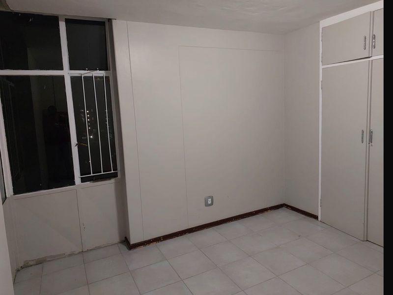 An empty bedroom featuring tiled flooring, a built-in wardrobe, and a window with security bars, offering a blank canvas for personalization.