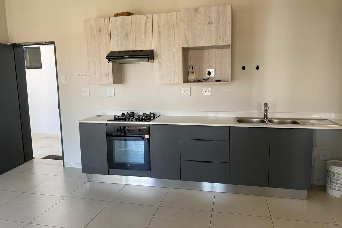 Modern kitchen featuring dark grey base cabinets, light wood-look upper cabinetry, stone countertops, and integrated gas hob and oven.