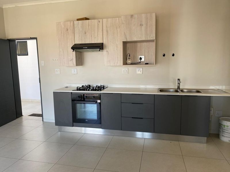 Modern kitchen featuring dark grey base cabinets, light wood-look upper cabinetry, stone countertops, and integrated gas hob and oven.