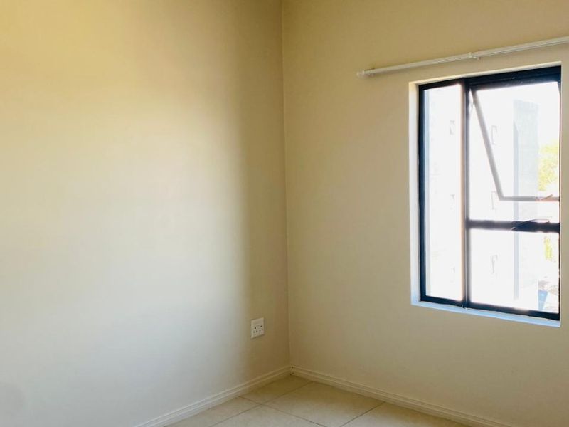 A clean, empty bedroom featuring neutral tiled flooring, a single casement window with a curtain rail, and plain walls.