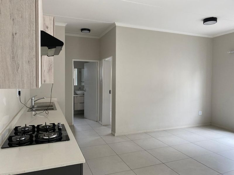 Modern open-plan kitchen and living area featuring tiled floors, built-in cabinetry, gas hob, and extractor fan, with a view into the adjacent bathroom.