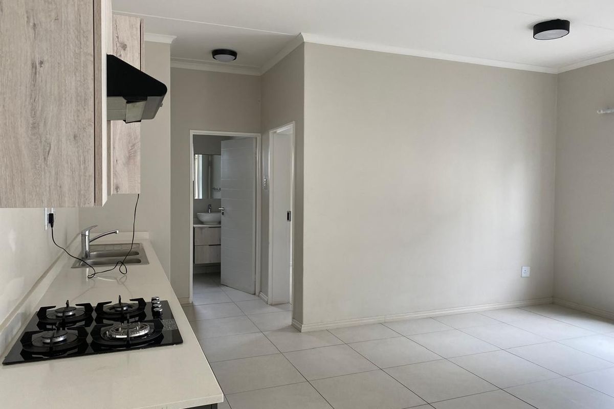 Modern open-plan kitchen and living area featuring tiled floors, built-in cabinetry, gas hob, and extractor fan, with a view into the adjacent bathroom.