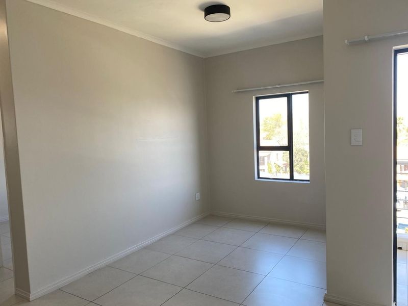 A bright, empty bedroom featuring neutral tiled flooring, clean walls, and a modern ceiling light fixture, offering a versatile space ready for personalization.