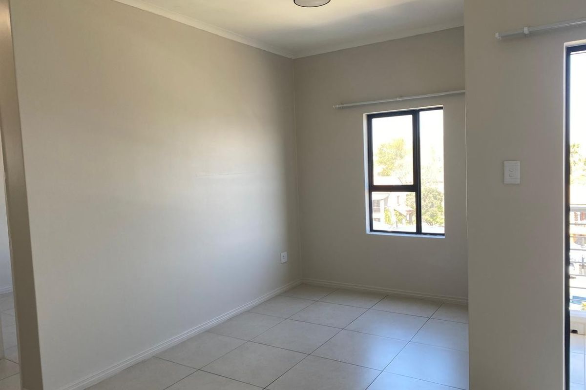 A bright, empty bedroom featuring neutral tiled flooring, clean walls, and a modern ceiling light fixture, offering a versatile space ready for personalization.