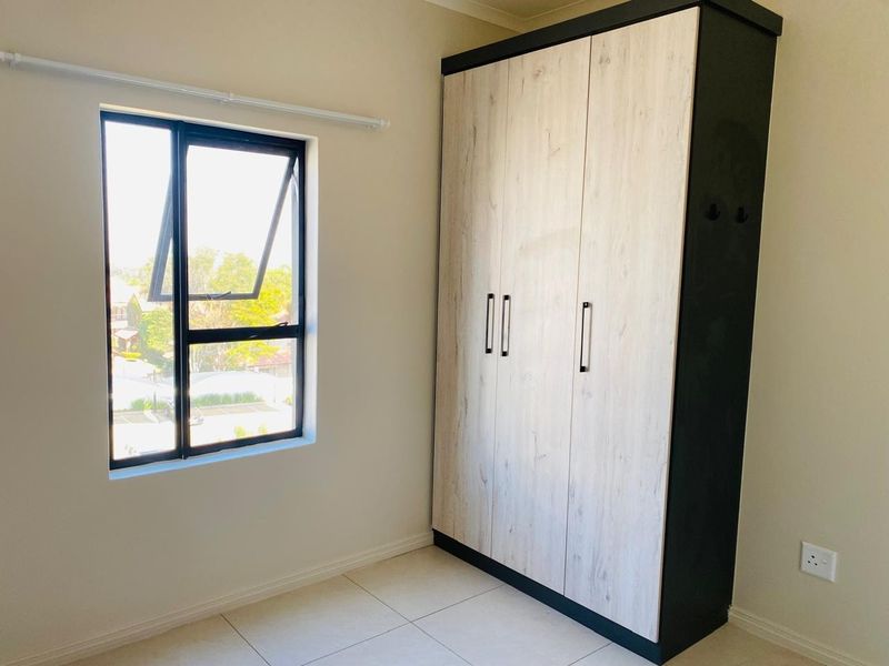 A bright, empty bedroom featuring modern tiled flooring, a large built-in wardrobe with wood-grain finish, and an aluminium-framed window.