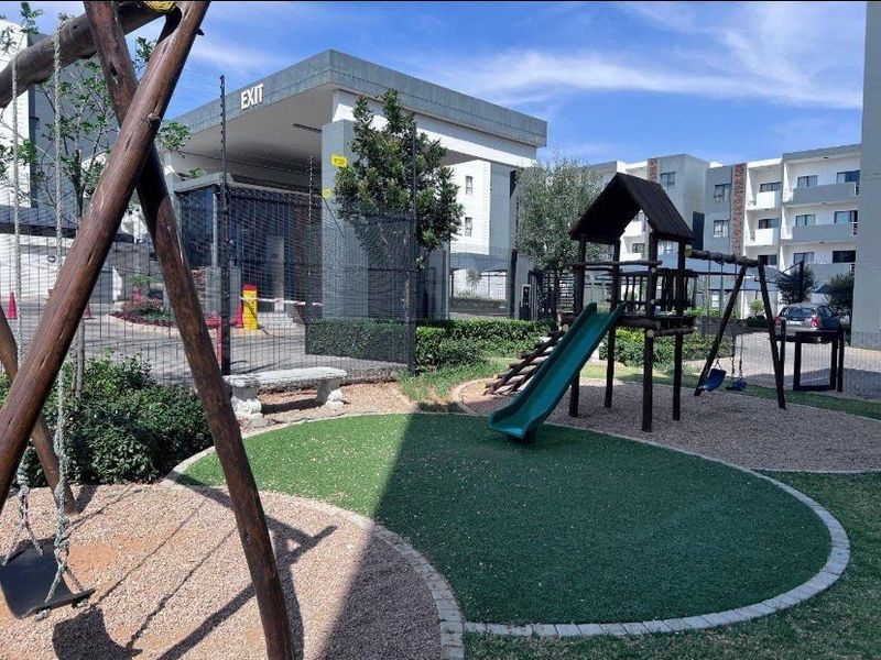 A well-maintained communal garden area featuring a children's playground with swings and a slide, set within a secure apartment complex.