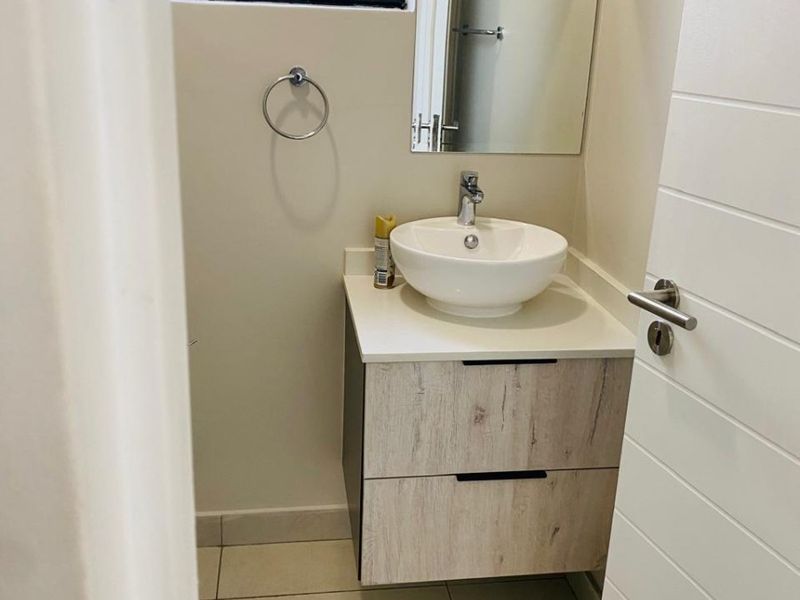 A compact, modern bathroom featuring a contemporary vessel sink, floating vanity cabinet, and neutral tiled flooring.