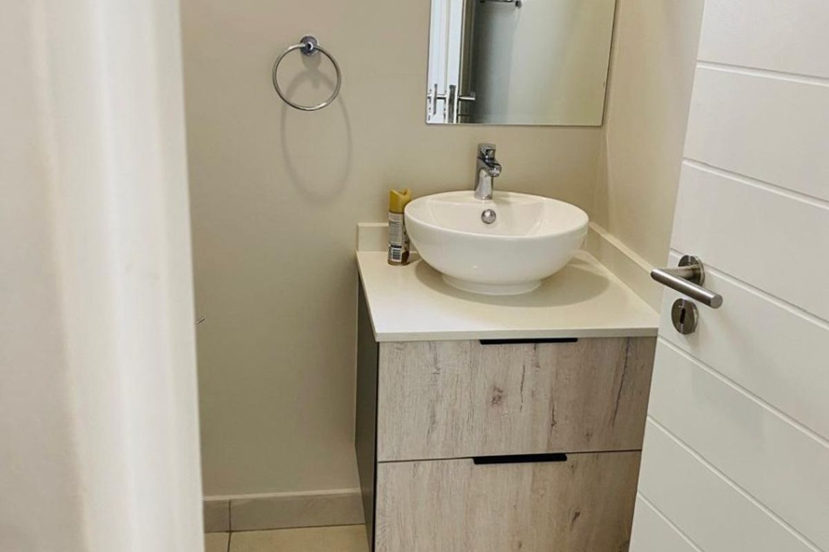 A compact, modern bathroom featuring a contemporary vessel sink, floating vanity cabinet, and neutral tiled flooring.