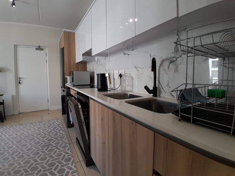 Modern kitchen featuring sleek white upper cabinets, wood-grain lower cabinetry, stone countertops, and a marble-look splashback with a contemporary black mixer tap.
