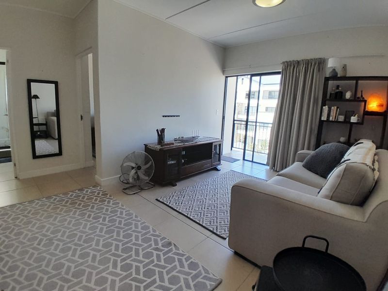 A bright living room featuring tiled flooring and a sliding glass door that opens onto a balcony, providing natural light and access to outdoor space.