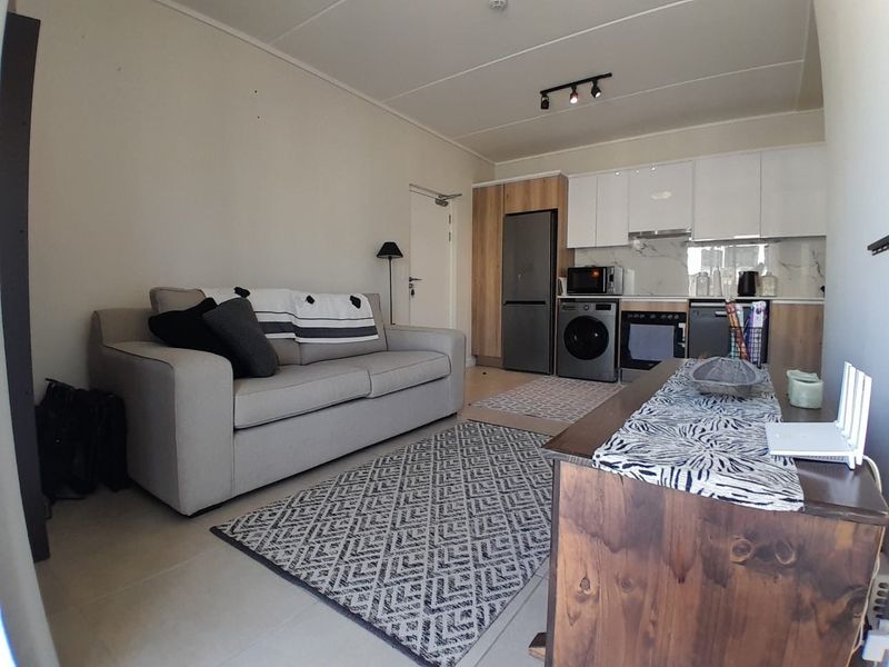 Modern open-plan living area featuring a compact kitchen with built-in cabinetry, integrated appliances, and sleek marble-look splashback, seamlessly connected to the lounge space.