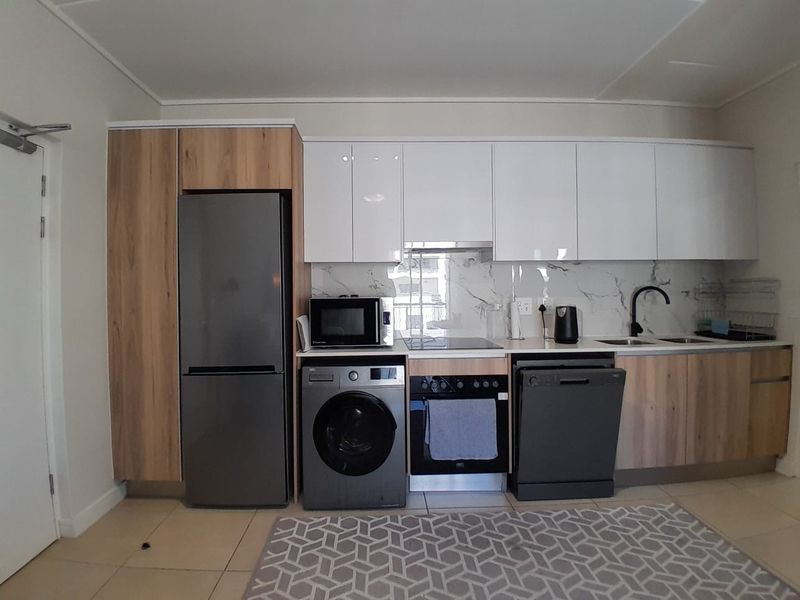 Modern kitchen featuring white and wood-grain cabinetry, marble-look splashback, integrated oven, hob, extractor fan, and stainless steel sink with contemporary fixtures.