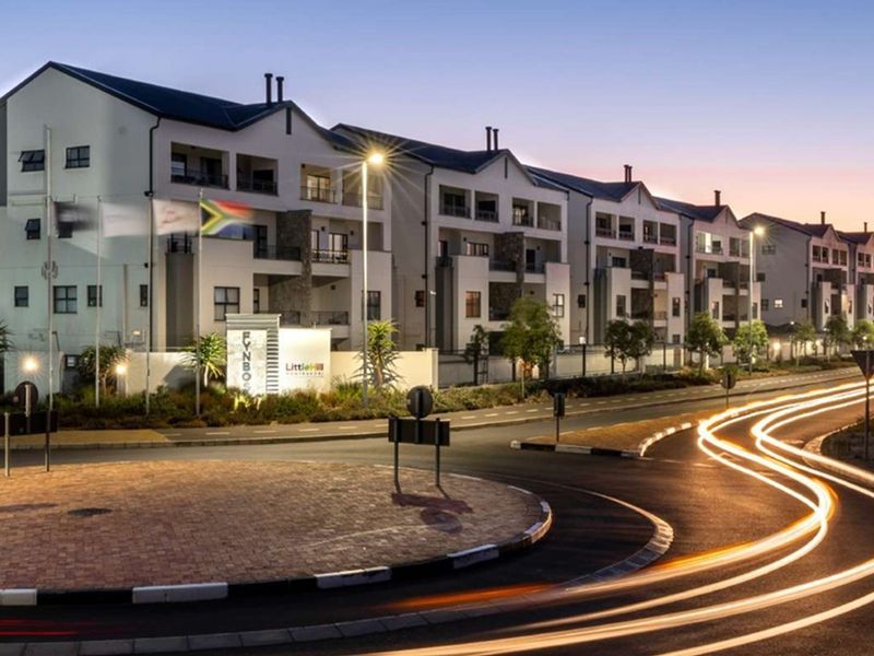 A professional evening view of the Fynbos apartment complex, showcasing the modern multi-story building facade, balconies, and surrounding landscaped grounds.