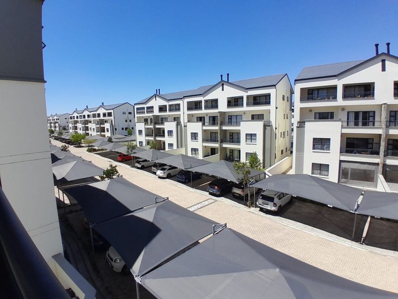 An elevated view of a modern apartment complex featuring paved parking areas with shade cloth carports and multi-story residential buildings.