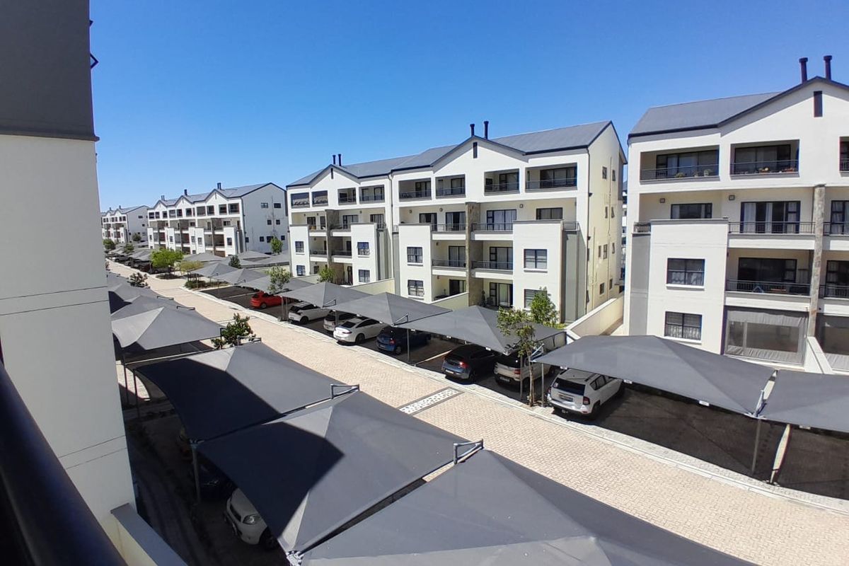 An elevated view of a modern apartment complex featuring paved parking areas with shade cloth carports and multi-story residential buildings.
