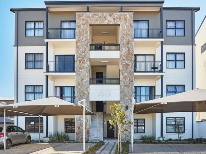 Front elevation of a modern multi-story apartment building featuring stone cladding, private balconies, and dedicated shaded parking bays.