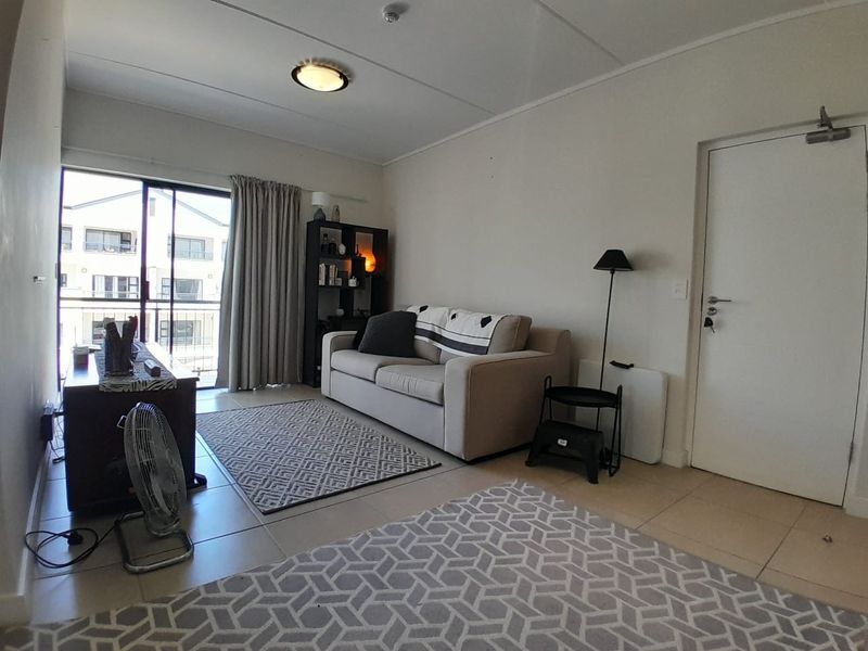 A living room featuring tiled flooring and a sliding glass door leading to a balcony, providing natural light to the space.