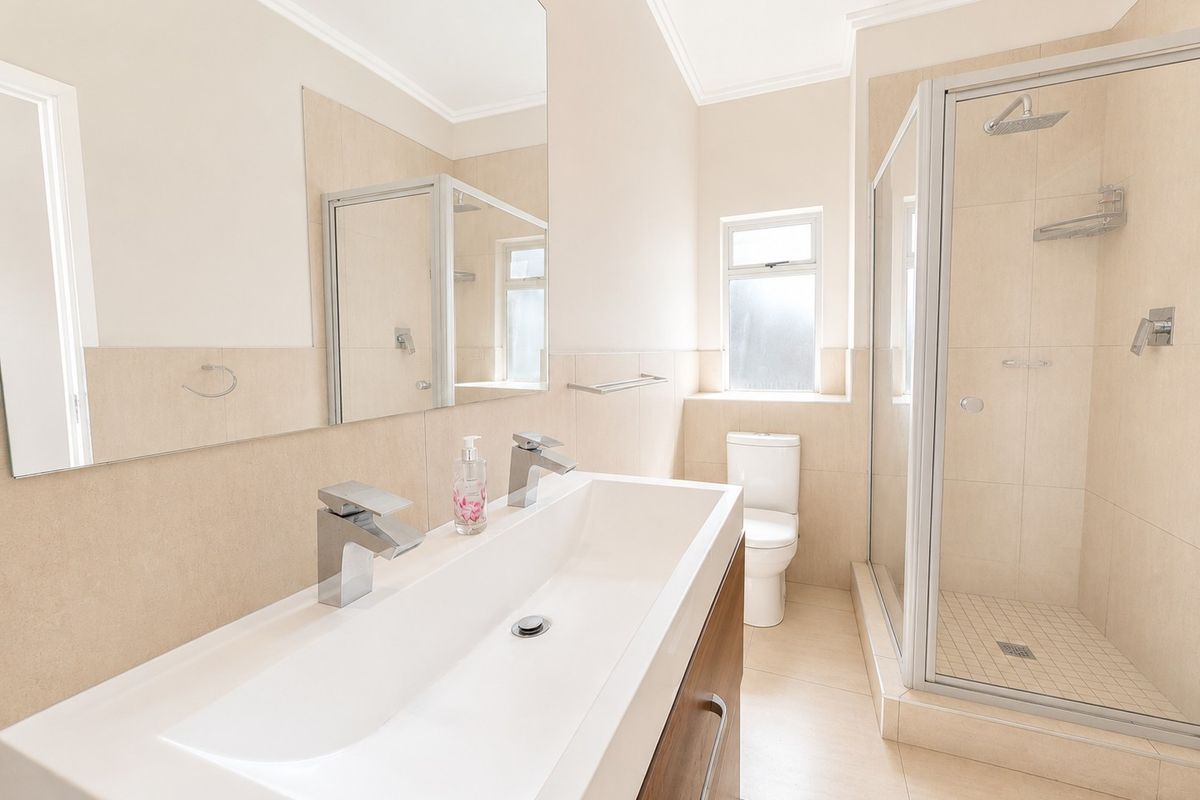 Modern bathroom featuring a double vanity, a glass-enclosed shower, and neutral tiled finishes throughout, offering a clean and functional space.