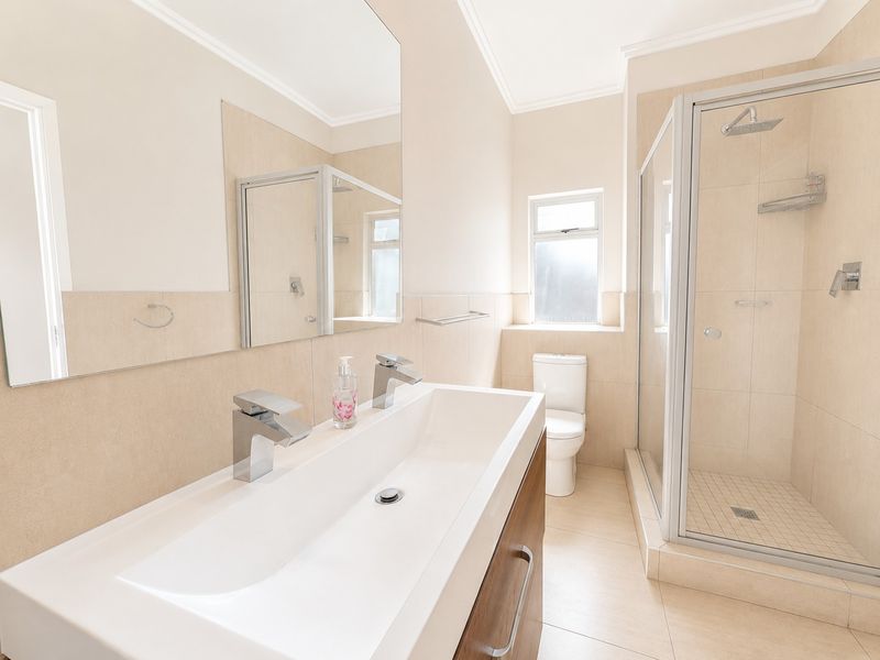 Modern bathroom featuring a double vanity, a glass-enclosed shower, and neutral tiled finishes throughout, offering a clean and functional space.