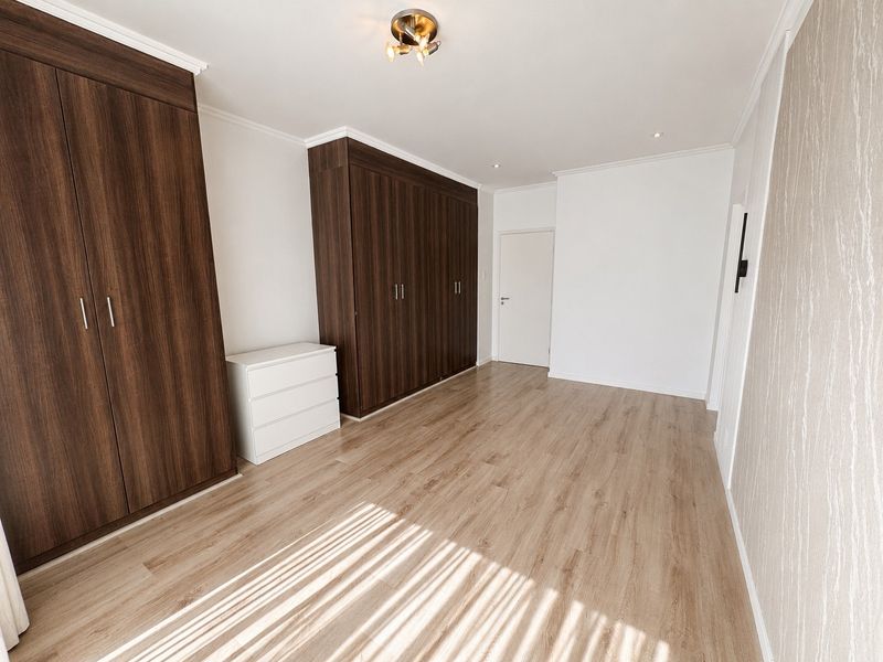 Spacious bedroom featuring light wood-look laminate flooring, extensive dark wood built-in cupboards, and a feature wall with textured wallpaper.