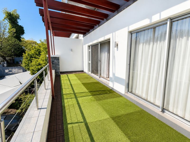 Spacious balcony featuring a timber pergola, artificial turf flooring, and stainless steel balustrades, providing a clean and modern outdoor living space.