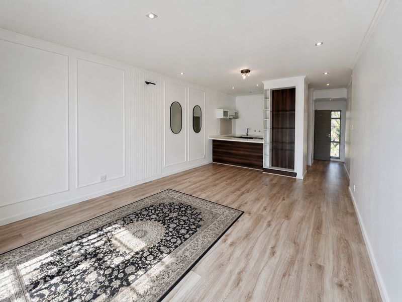 Spacious open-plan living area featuring modern laminate flooring, elegant wall paneling, recessed lighting, and a compact kitchen with built-in cabinetry.