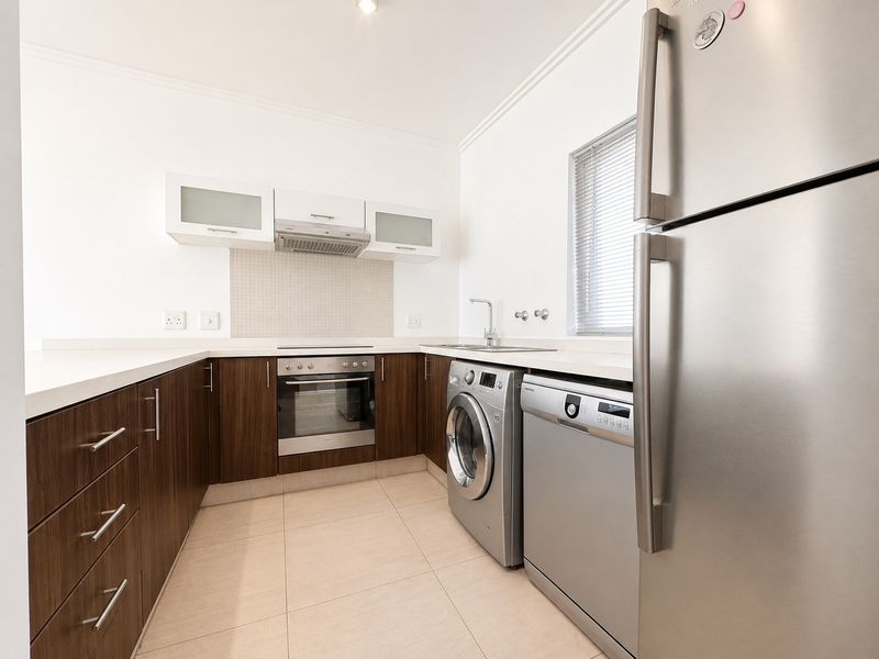 Modern kitchen featuring dark wood cabinetry, stone countertops, tiled backsplash, and integrated stainless steel appliances.