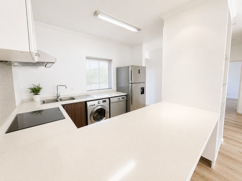 Modern kitchen featuring clean white cabinetry, quartz countertops, an electric hob, and integrated space for laundry appliances.