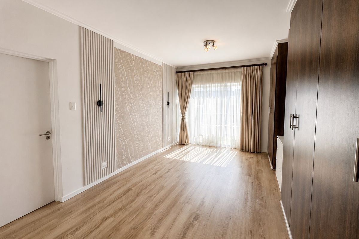 A bright, modern bedroom featuring wood-look laminate flooring, built-in cabinetry, and a stylish feature wall with integrated lighting.