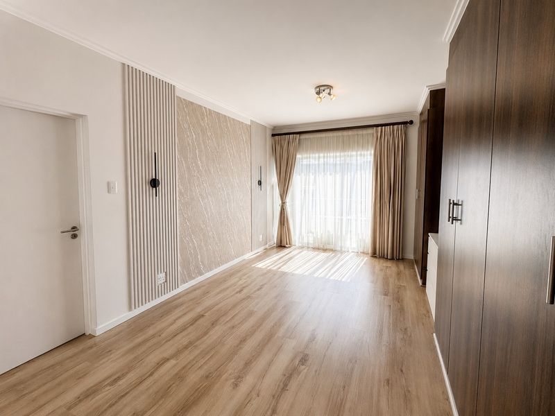 A bright, modern bedroom featuring wood-look laminate flooring, built-in cabinetry, and a stylish feature wall with integrated lighting.