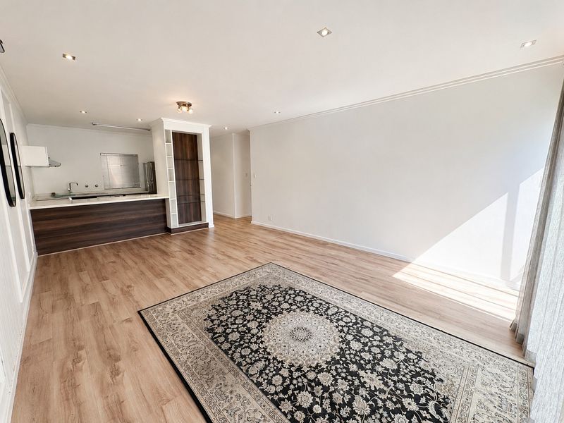 Spacious open-plan living area featuring modern laminate flooring, recessed lighting, and a functional kitchen with built-in cabinetry and island.