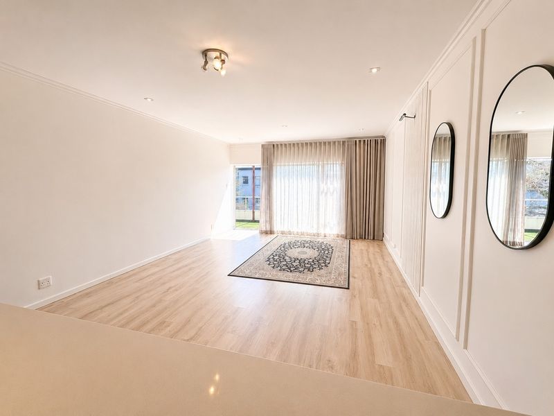 Spacious, light-filled living area featuring modern laminate flooring, elegant wainscoting, and large sliding glass doors leading to an outdoor space.