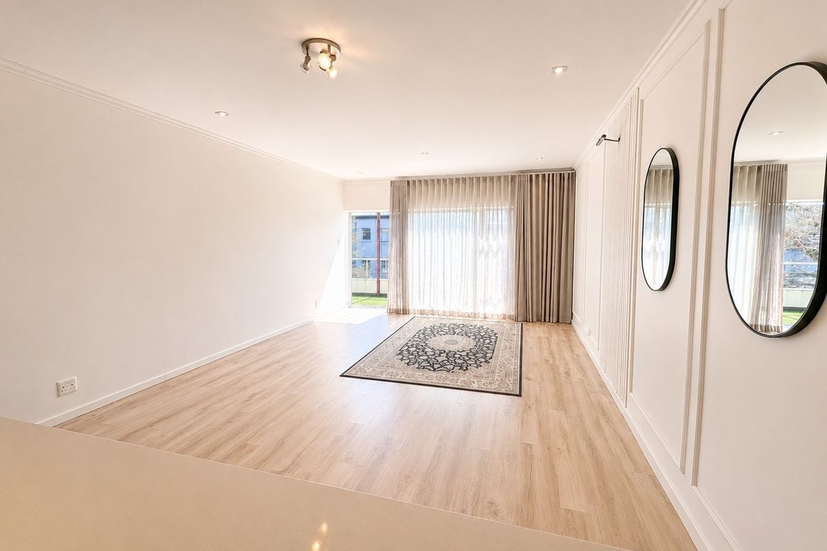 Spacious, light-filled living area featuring modern laminate flooring, elegant wainscoting, and large sliding glass doors leading to an outdoor space.