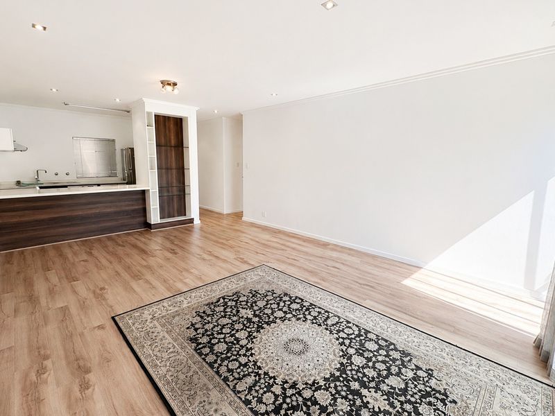 Spacious open-plan living area featuring modern laminate flooring, recessed lighting, and a functional kitchen with built-in cabinetry and shelving.