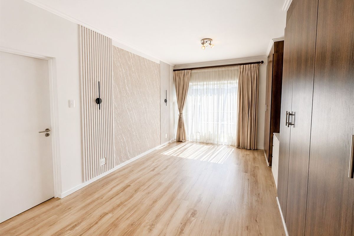 A bright, modern bedroom featuring wood-look laminate flooring, built-in cabinetry, and a decorative feature wall with integrated lighting.