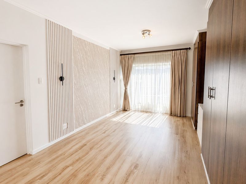 A bright, modern bedroom featuring wood-look laminate flooring, built-in cabinetry, and a decorative feature wall with integrated lighting.