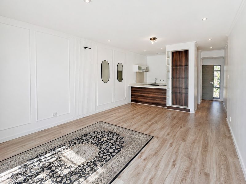 An open-plan living and kitchen area featuring modern laminate flooring, decorative wall paneling, recessed lighting, and built-in kitchen cabinetry.