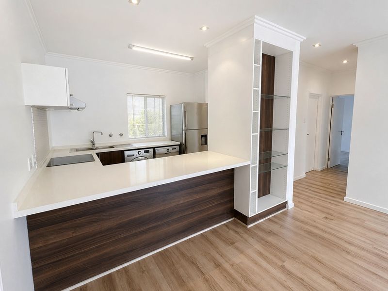Modern open-plan kitchen featuring sleek dark wood cabinetry, white quartz countertops, integrated shelving, and high-quality laminate flooring in a bright, well-lit space.