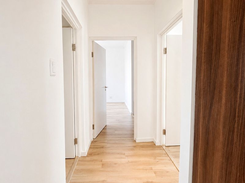 A bright, clean hallway featuring light wood-look laminate flooring and neutral white walls, providing access to multiple rooms within the apartment.