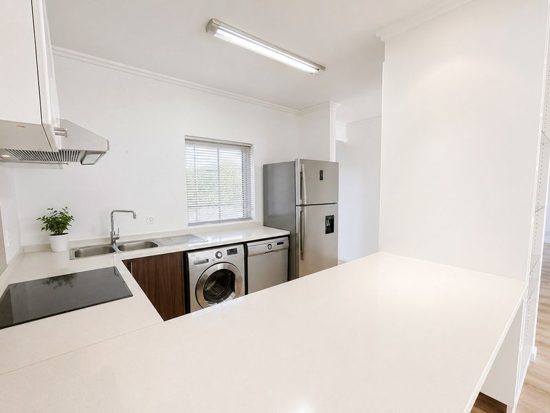 Modern kitchen featuring stone countertops, built-in cabinetry, integrated laundry plumbing, and a sleek electric hob with an overhead extractor fan.