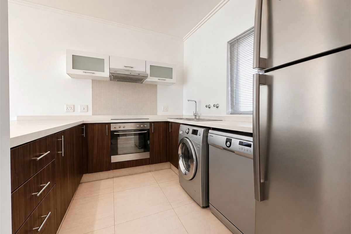Modern kitchen featuring dark wood cabinetry, stone countertops, built-in oven with extractor fan, and integrated plumbing for laundry and dishwasher appliances.