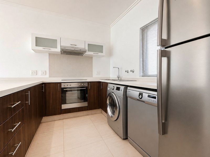 Modern kitchen featuring dark wood cabinetry, stone countertops, built-in oven with extractor fan, and integrated plumbing for laundry and dishwasher appliances.