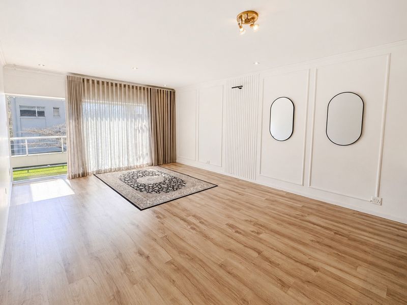 Bright and spacious living area featuring modern laminate flooring, elegant wainscoting, slatted wall detailing, and direct access to a private balcony.