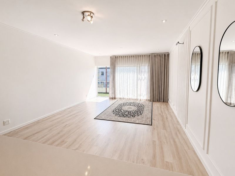 A bright and spacious living area featuring light-toned laminate flooring, elegant wainscoting, and large sliding glass doors that provide ample natural light.