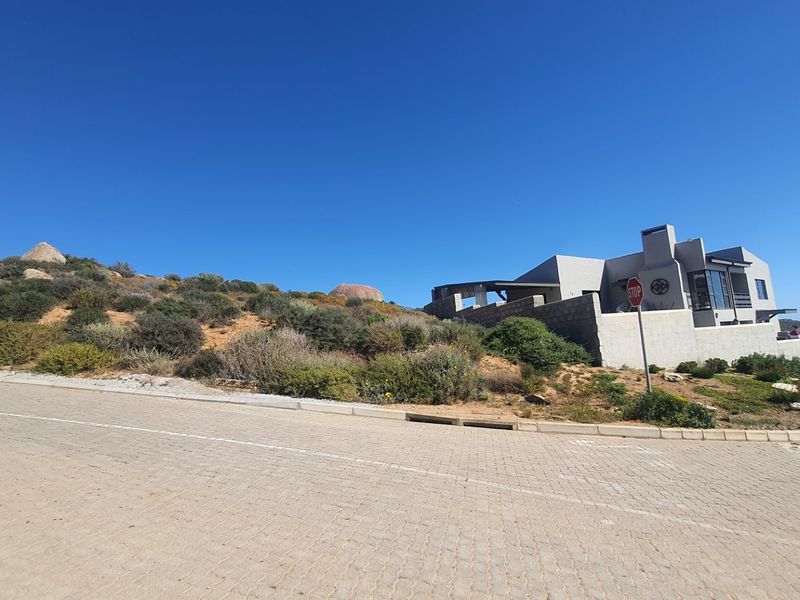 A street-level view of a residential property situated on a sloped lot, featuring a paved road and a modern architectural structure.