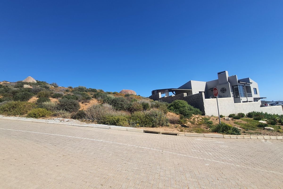 A street-level view of a residential property situated on a sloped lot, featuring a paved road and a modern architectural structure.