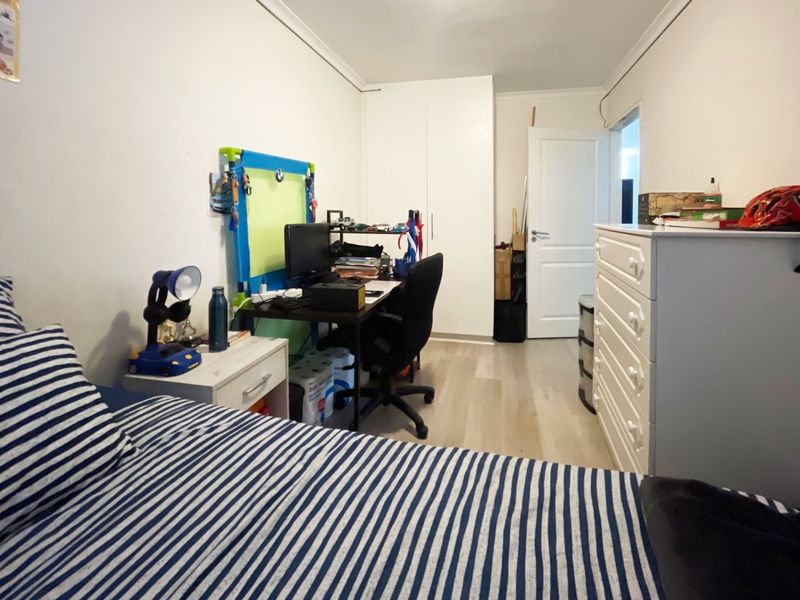 A functional bedroom featuring light-toned laminate flooring, a built-in wardrobe, and neutral wall finishes, offering a practical space for rest or study.