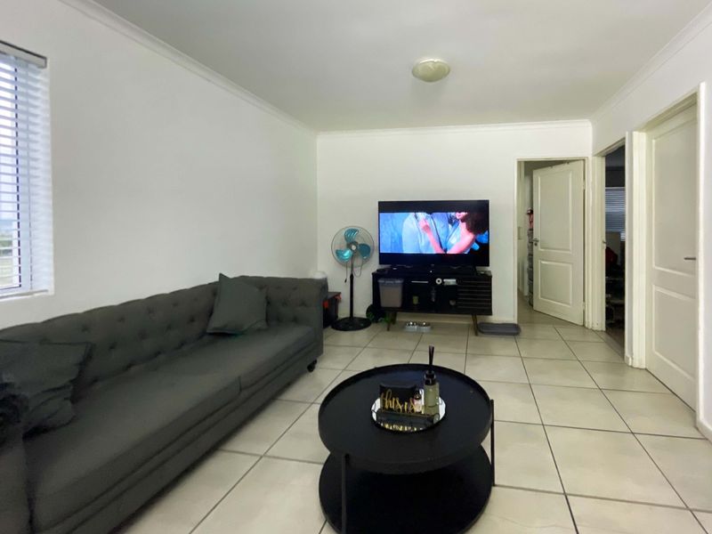 A functional living room featuring neutral tiled flooring, white walls, and venetian blinds, providing a clean and versatile space for relaxation.