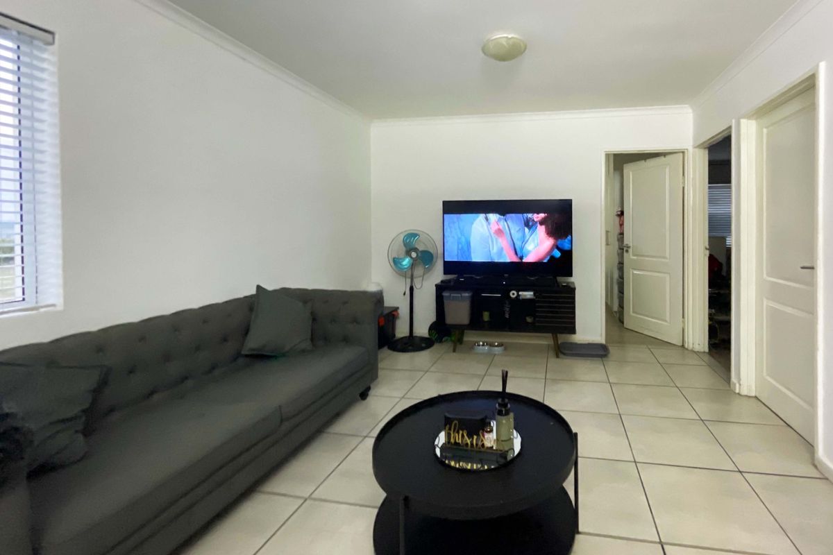 A functional living room featuring neutral tiled flooring, white walls, and venetian blinds, providing a clean and versatile space for relaxation.