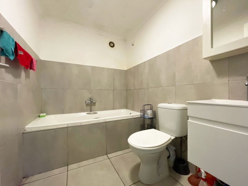 A functional bathroom featuring a bathtub, toilet, and vanity with wall-to-wall tiling.
